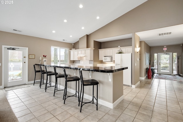 kitchen featuring light tile patterned floors, white appliances, visible vents, and a kitchen breakfast bar