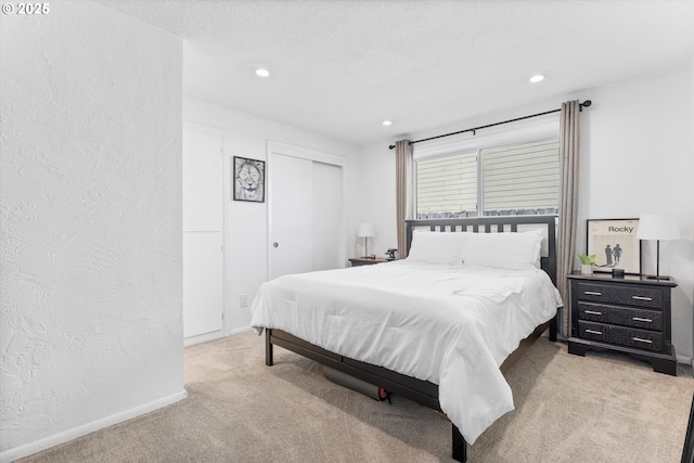 bedroom featuring a textured wall, recessed lighting, light colored carpet, baseboards, and a closet