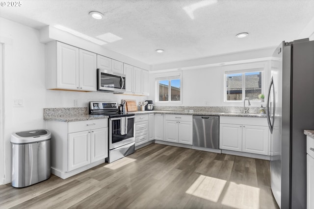 kitchen featuring appliances with stainless steel finishes, white cabinets, a sink, and wood finished floors