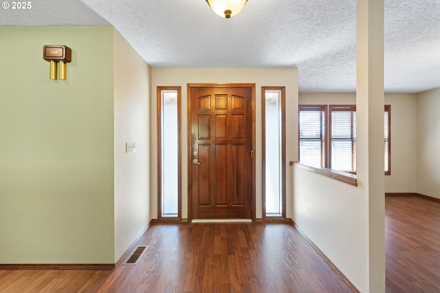 entryway with dark wood finished floors, baseboards, a textured ceiling, and visible vents