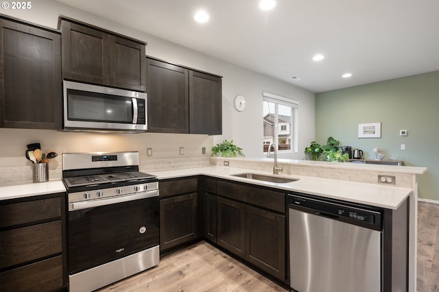 kitchen with a sink, appliances with stainless steel finishes, a peninsula, and light wood finished floors