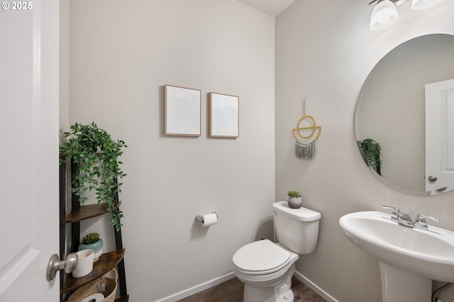 half bath with toilet, wood finished floors, baseboards, and a sink