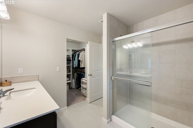 bathroom featuring vanity, a spacious closet, a shower stall, and a textured ceiling