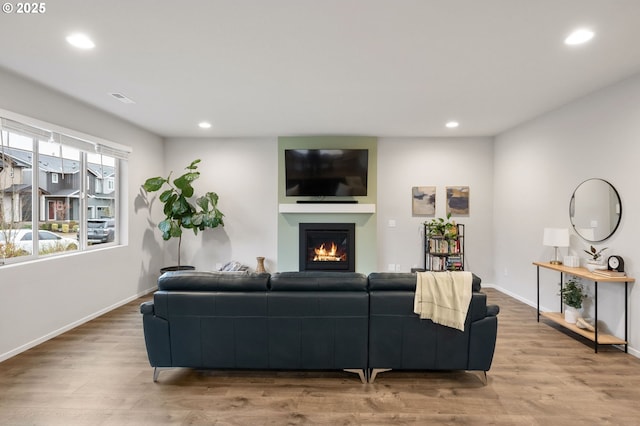 living area with recessed lighting, baseboards, wood finished floors, and a glass covered fireplace