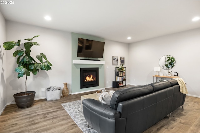 living area with a glass covered fireplace, baseboards, wood finished floors, and recessed lighting