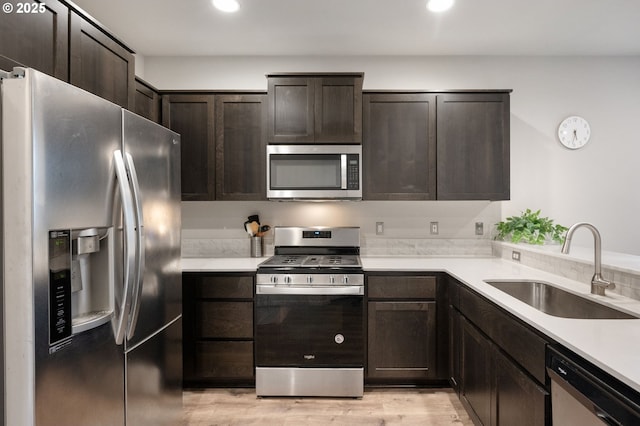 kitchen featuring a sink, stainless steel appliances, light countertops, dark brown cabinets, and light wood-style floors