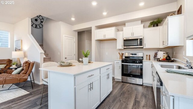 kitchen featuring stainless steel appliances, a sink, a breakfast bar, dark wood-style flooring, and white cabinets