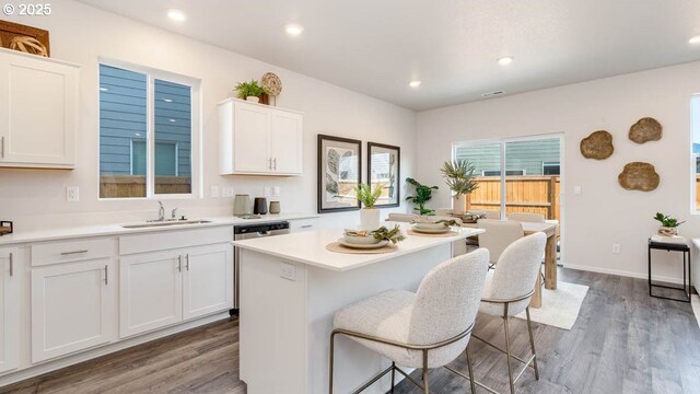 kitchen with a sink, wood finished floors, a kitchen bar, white cabinetry, and light countertops