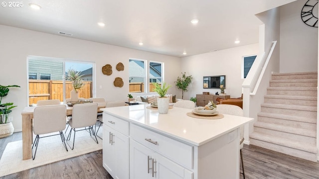 kitchen with open floor plan, wood finished floors, white cabinets, a center island, and light countertops