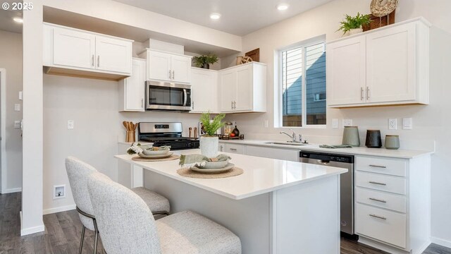 kitchen featuring appliances with stainless steel finishes, a sink, dark wood-type flooring, white cabinets, and recessed lighting