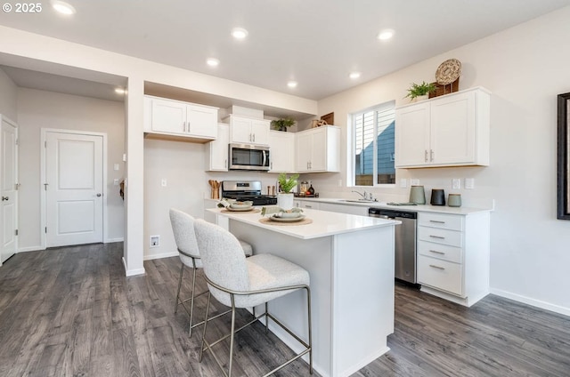 kitchen featuring stainless steel appliances, a sink, dark wood finished floors, white cabinetry, and a kitchen island
