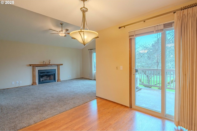 unfurnished living room featuring a fireplace with flush hearth, a healthy amount of sunlight, wood finished floors, and vaulted ceiling