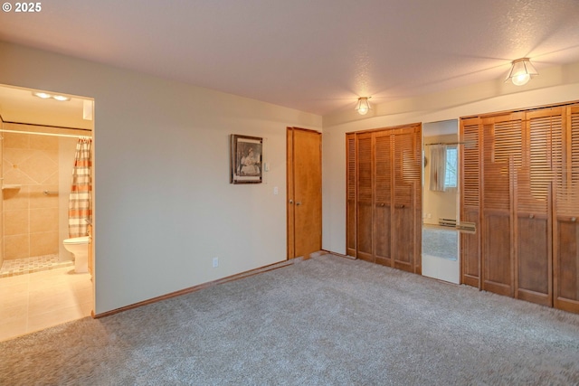 unfurnished bedroom featuring ensuite bathroom, multiple closets, carpet floors, and a baseboard radiator