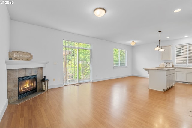 4345 SW Vino Pl, Beaverton, OR 97078 - unfurnished living room with light wood finished floors, a tiled fireplace, baseboards, recessed lighting, and a sink