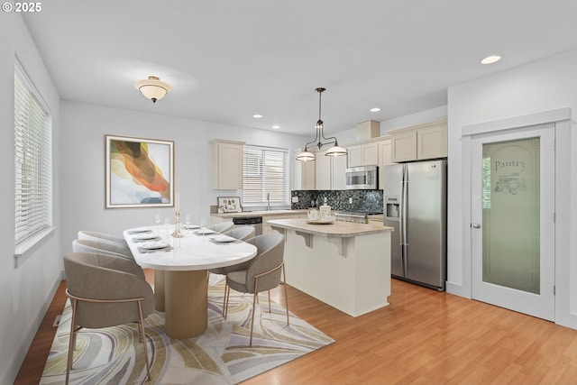 4345 SW Vino Pl, Beaverton, OR 97078 - kitchen with stainless steel appliances, a kitchen bar, light wood-type flooring, light countertops, and decorative backsplash