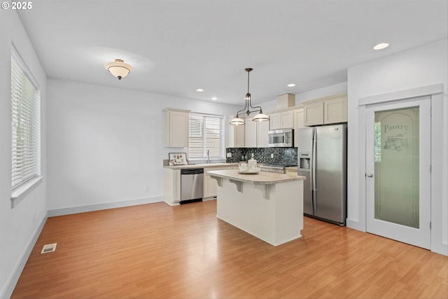 4345 SW Vino Pl, Beaverton, OR 97078 - kitchen with stainless steel appliances, a kitchen breakfast bar, light wood-style floors, light countertops, and backsplash