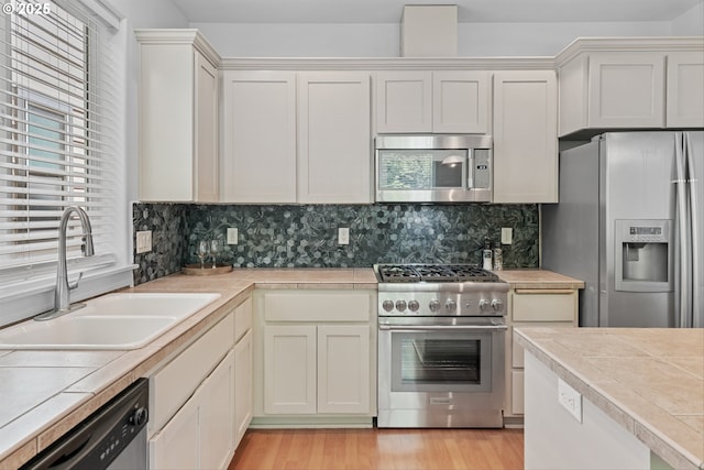 4345 SW Vino Pl, Beaverton, OR 97078 - kitchen featuring appliances with stainless steel finishes, a sink, tasteful backsplash, light wood finished floors, and tile counters