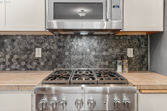 4345 SW Vino Pl, Beaverton, OR 97078 - kitchen featuring stainless steel microwave, backsplash, white cabinets, stove, and tile counters