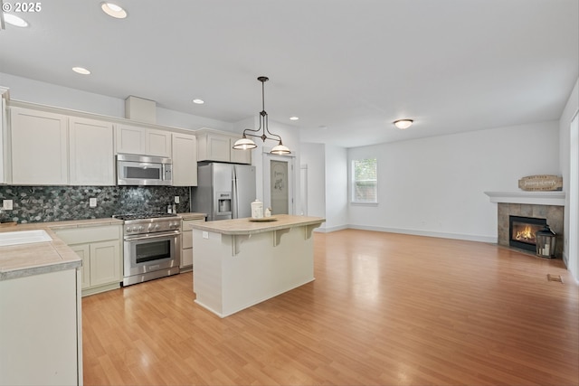 4345 SW Vino Pl, Beaverton, OR 97078 - kitchen with stainless steel appliances, light countertops, open floor plan, light wood-style floors, and a kitchen bar
