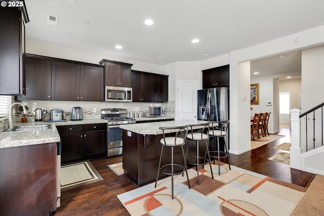 kitchen with sink, a breakfast bar area, a center island, stainless steel appliances, and dark wood-type flooring