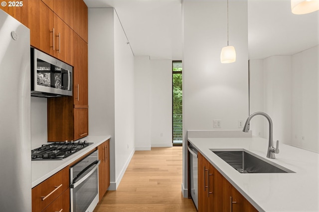 922 NW 11th Ave Unit 209, Portland, OR 97209 - kitchen with stainless steel appliances, brown cabinets, light wood finished floors, light countertops, and hanging light fixtures