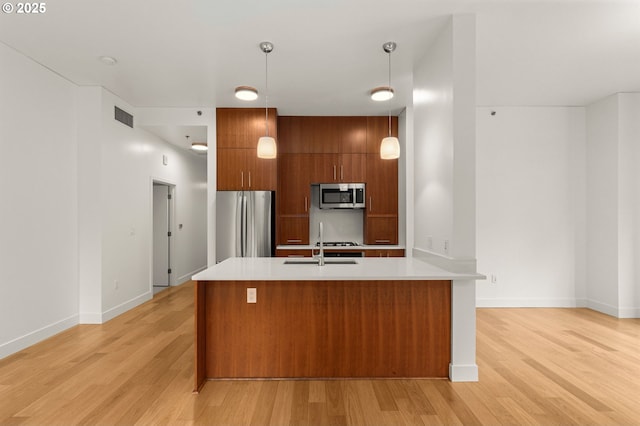 922 NW 11th Ave Unit 209, Portland, OR 97209 - kitchen featuring stainless steel appliances, brown cabinets, light countertops, light wood-type flooring, and decorative light fixtures