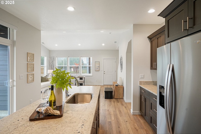 kitchen featuring light wood-style floors, light stone counters, stainless steel refrigerator with ice dispenser, and a sink