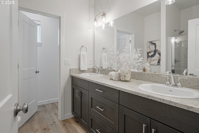 bathroom featuring wood finished floors, double vanity, a sink, and walk in shower