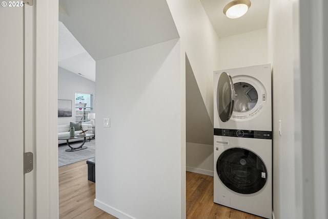 laundry area featuring laundry area, stacked washing maching and dryer, wood finished floors, and baseboards