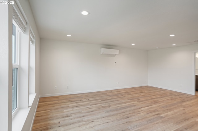 spare room featuring baseboards, an AC wall unit, light wood-type flooring, and recessed lighting