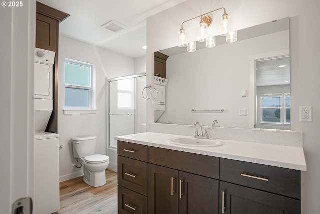 full bath featuring toilet, wood finished floors, visible vents, stacked washer / drying machine, and a shower stall