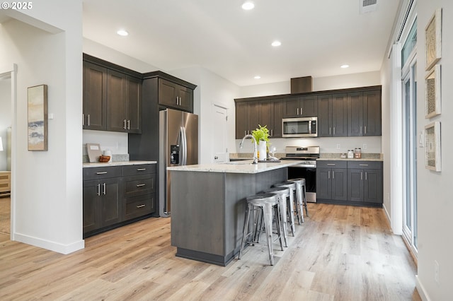 kitchen featuring light wood-style flooring, appliances with stainless steel finishes, a breakfast bar, and recessed lighting