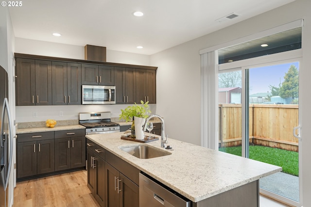 kitchen featuring visible vents, light stone countertops, stainless steel appliances, light wood-type flooring, and a sink