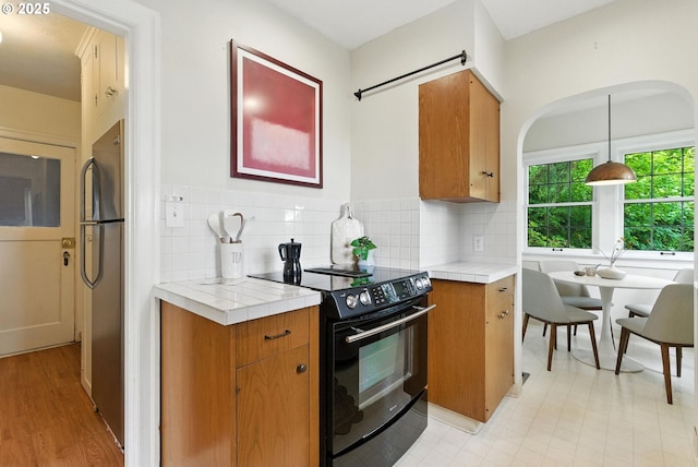 368 NW Lomita Ter, Portland, OR 97210 - kitchen featuring black electric range oven, freestanding refrigerator, tile counters, and brown cabinetry
