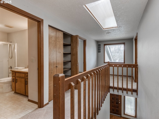 corridor featuring light colored carpet, a textured ceiling, and a skylight