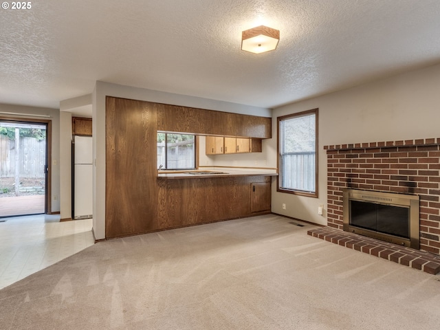 unfurnished living room with a fireplace, light colored carpet, a textured ceiling, and plenty of natural light