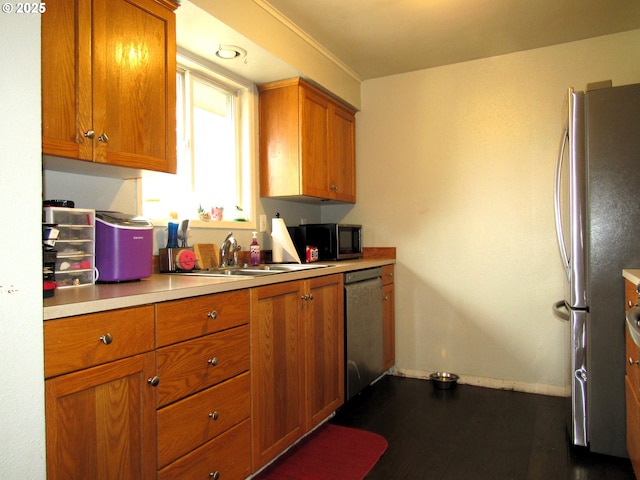 kitchen featuring stainless steel appliances, light countertops, brown cabinetry, a sink, and baseboards