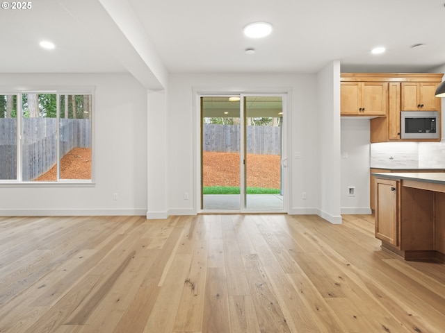 kitchen featuring light wood finished floors, stainless steel microwave, a healthy amount of sunlight, and baseboards