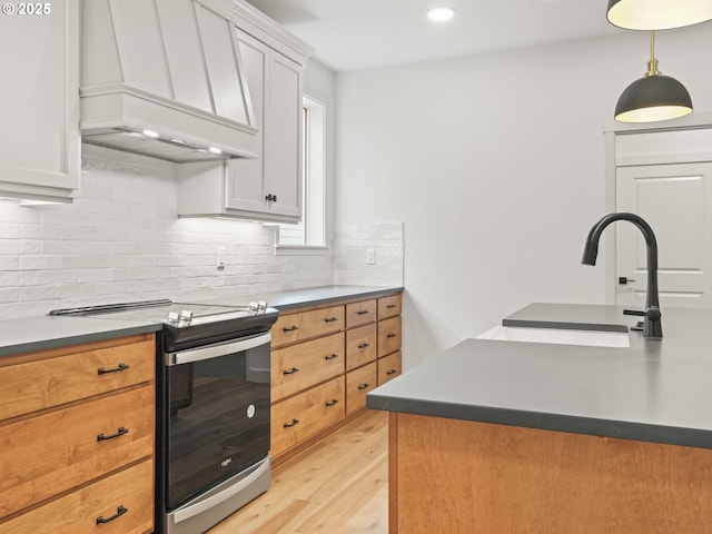 kitchen with stainless steel electric range oven, custom exhaust hood, light wood-style flooring, a sink, and backsplash