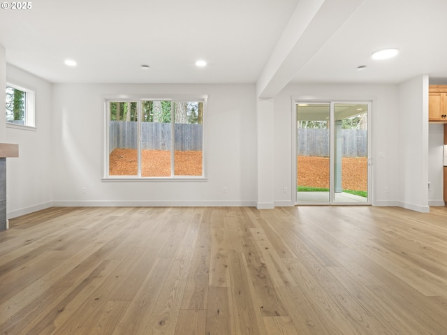 unfurnished living room featuring a fireplace, light wood-type flooring, a wealth of natural light, and baseboards