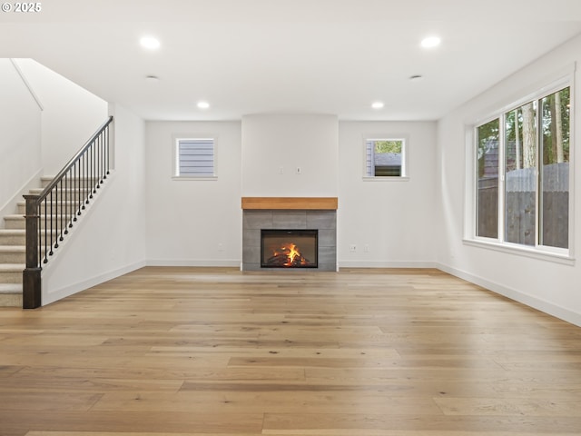 unfurnished living room with stairs, a tiled fireplace, light wood-style flooring, and recessed lighting