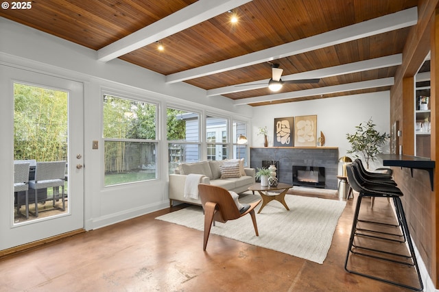 living area featuring finished concrete floors, beamed ceiling, wooden ceiling, and a glass covered fireplace