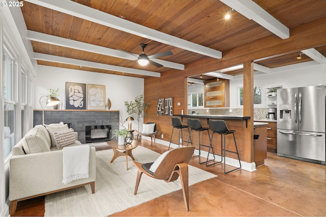 living area with ceiling fan, concrete flooring, a glass covered fireplace, wooden ceiling, and beamed ceiling