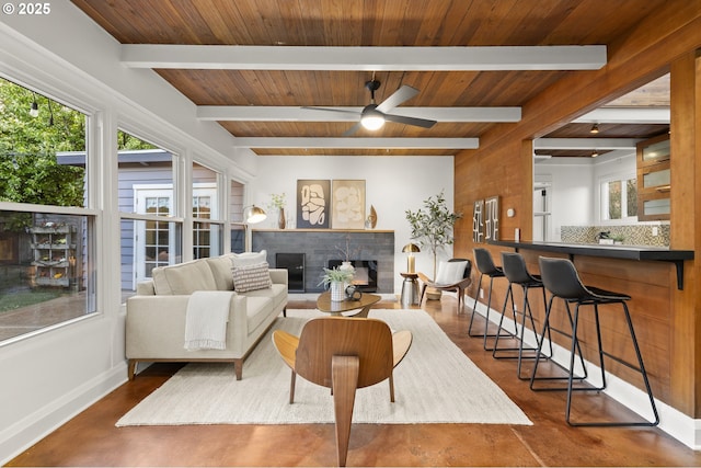 living room with baseboards, beamed ceiling, ceiling fan, wood ceiling, and a brick fireplace