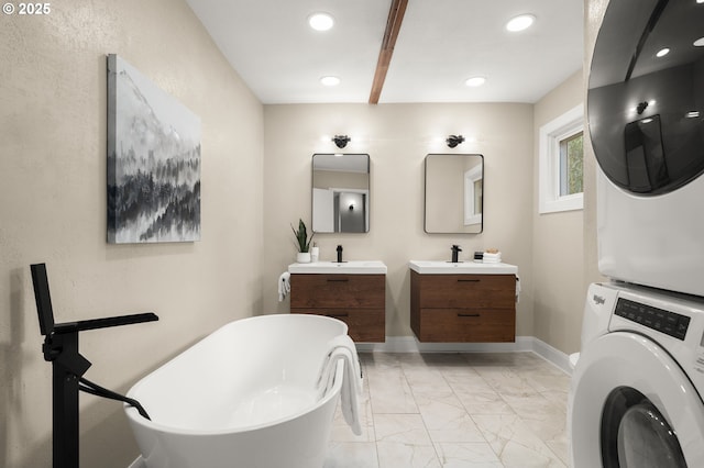 full bathroom featuring a freestanding tub, two vanities, marble finish floor, stacked washer / dryer, and baseboards