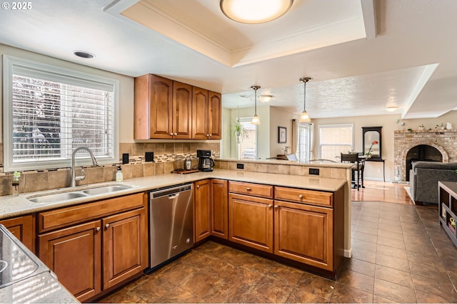 kitchen with dishwasher, brown cabinets, a peninsula, a tray ceiling, and a sink