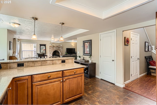 kitchen with a textured ceiling, a fireplace, hanging light fixtures, brown cabinets, and light stone countertops