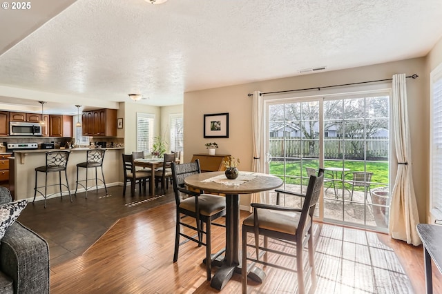 dining room featuring visible vents, a textured ceiling, baseboards, and wood finished floors