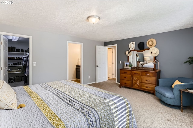 bedroom with carpet, a walk in closet, a closet, a textured ceiling, and baseboards