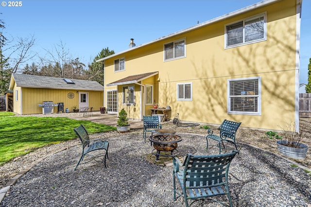 rear view of house featuring an outbuilding, a patio, an outdoor fire pit, fence, and a yard